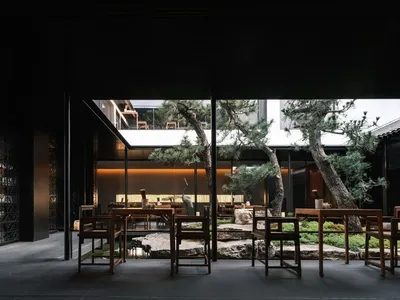 Modern restaurant courtyard with wooden tables, glass walls, and stone elements.