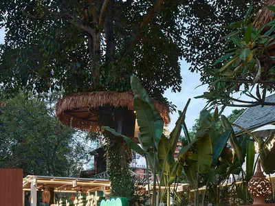 A modern restaurant with brick stairs and tropical plants, featuring a treehouse-like structure.