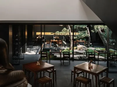Modern, minimalist restaurant interior with wooden furniture and a serene outdoor courtyard.