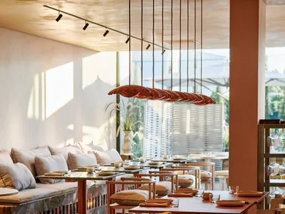 Modern restaurant interior with wooden tables, cushioned chairs, and warm lighting.