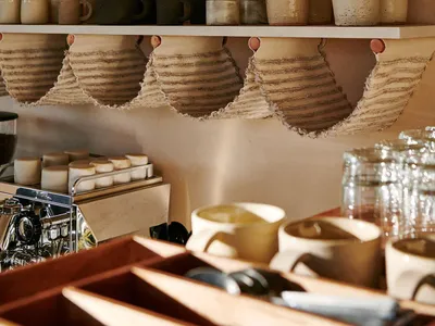 Ceramic cups, mugs, and vases neatly arranged on open shelves in a coffee shop interior.