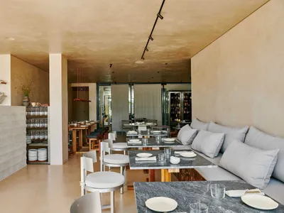 A modern restaurant interior featuring concrete walls and floors with tables set for dining.