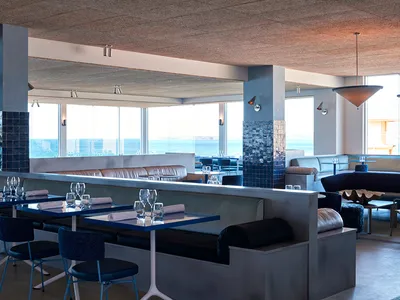 Modern restaurant interior with concrete walls, glass windows, and leather seating