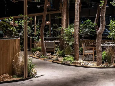 Indoor restaurant space featuring industrial design elements such as concrete floors, exposed beams, and plant-filled seating