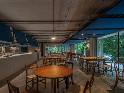 A modern restaurant dining area with concrete floors and wooden tables and chairs.