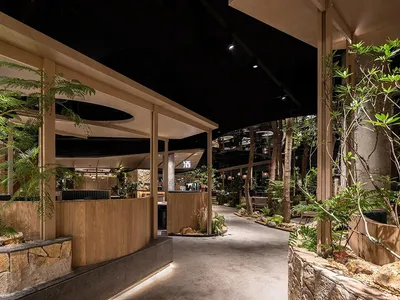 Modern restaurant interior with wooden features, stone elements, and lush greenery.