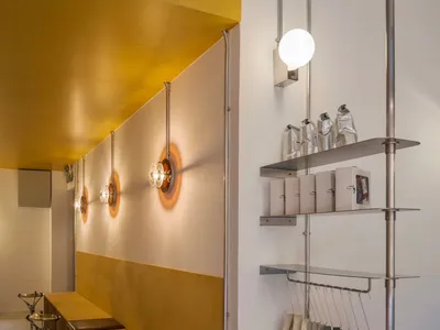 Modern cafe interior with wooden benches, concrete floor, and hanging lamps.