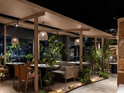 Industrial restaurant interior with concrete and wood materials, natural-fiber pendant lights, and green plants.