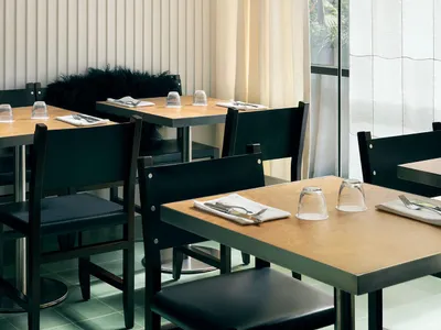 An image of an industrial-style restaurant interior with wooden tables, glassware, and metal chairs.