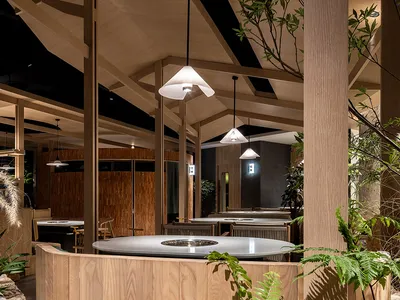 A modern restaurant interior featuring wooden tables and hanging lights.