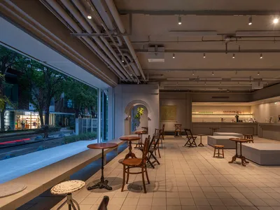 Modern minimalist restaurant interior with concrete walls, wooden tables, and industrial lighting.