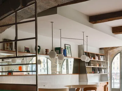 A modern restaurant bar with concrete walls, wooden stools, and tiled floor