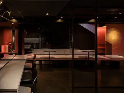 Modern restaurant interior with concrete finishes, glass partitions, and wooden seating.