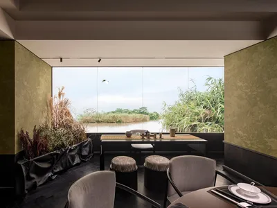 Modern restaurant interior with wooden table and chairs, overlooking a serene lake.