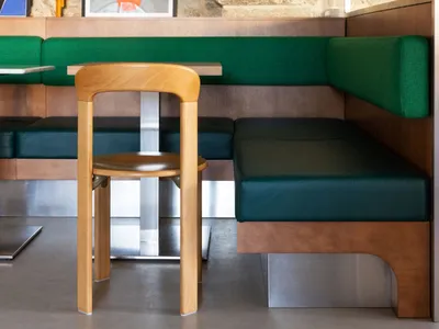 Modern restaurant interior featuring a contemporary seating area with wooden stools and upholstered booths, set against rusti