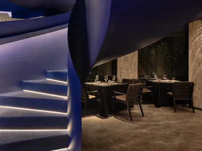 A modern restaurant interior featuring a curved, illuminated blue staircase.