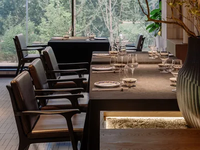 A modern restaurant interior with sleek, minimalist design and large windows showcasing a green outdoor environment.