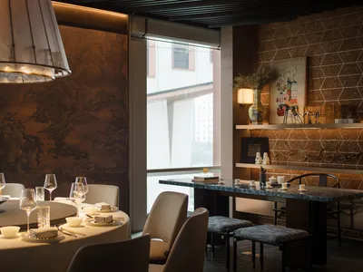 A contemporary restaurant interior with metallic walls, carpeted flooring, and stone tables.