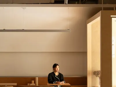 A person sitting alone at a table in a cafe with wooden furniture and minimalist design.