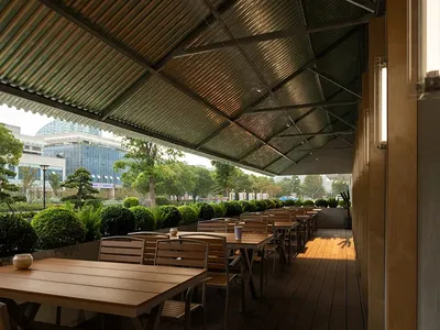 Outdoor seating area of a modern restaurant featuring wooden tables, concrete flooring, and greenery.