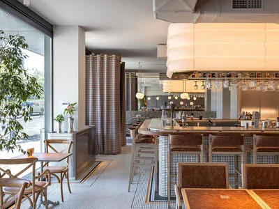 Interior of a cafe featuring wooden tables, leather chairs, glass drinkware, and a metal bar top.