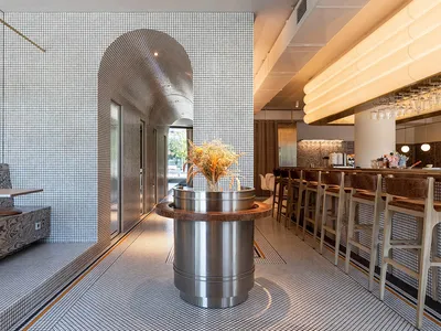 Modern cafe bar interior with metallic structures, ceramic tile floors, and wooden seating.
