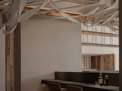 A minimalist restaurant interior featuring a bar counter with a concrete surface and wooden chairs.