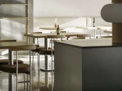 A modern restaurant interior featuring minimalist design, wooden tables, and concrete finishes.