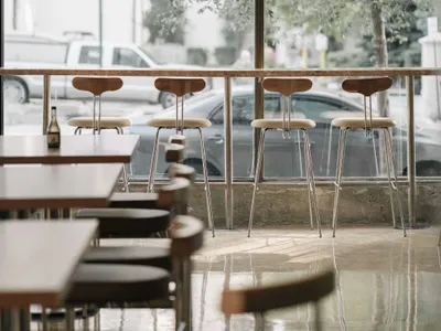 A modern restaurant bar area featuring white pendant lights, teak bar stools, and a sleek counter.