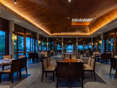 A spacious, modern restaurant interior with wood finishes and numerous dining tables.