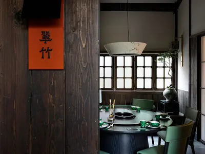 A modern restaurant interior featuring wooden materials and a round dining table with green chairs.