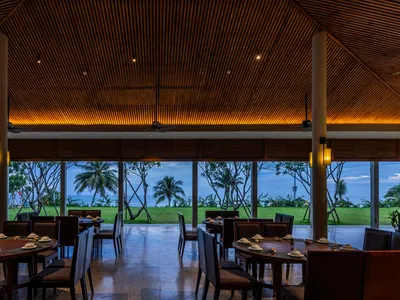A modern restaurant interior with wooden ceiling and glass walls overlooking the coast.
