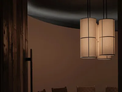 Modern restaurant dining room with round wooden table, leather chairs, and cylindrical pendant lights.