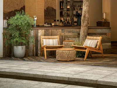 A modern restaurant bar with concrete walls, wooden furniture, and plants.