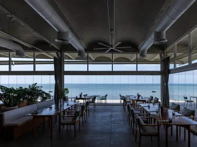 An industrial-style restaurant with a sea view, featuring concrete and glass materials.