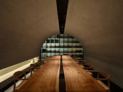 A modern restaurant interior featuring wooden tables and chairs in a tunnel-like space