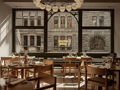 Interior view of a modern cafe featuring wooden seating and large windows overlooking a stone building.