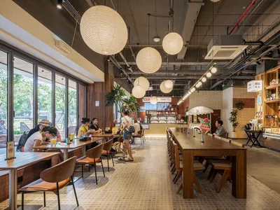 A cozy cafe interior with wooden tables, paper lanterns, and potted plants.