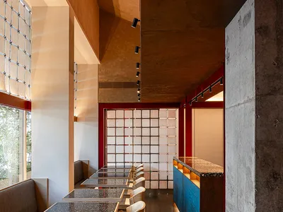 An industrial-style restaurant interior with concrete walls, glass partitions, and wooden furniture.