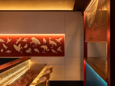 Modern restaurant bar featuring a metallic desk and illuminated wall art with bird illustrations.