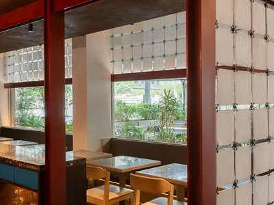 Interior view of a modern restaurant with wooden tables, concrete walls, and glass dividers.