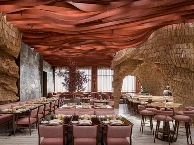 Modern restaurant interior with wooden ceiling and stone walls, featuring multiple dining tables and chairs.