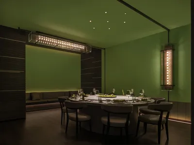 A modern restaurant dining room with dark green walls and illuminated lighting.