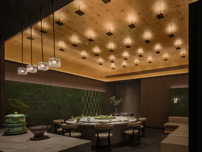 A modern restaurant with marble and concrete walls, featuring a large dining table and pendant lights.