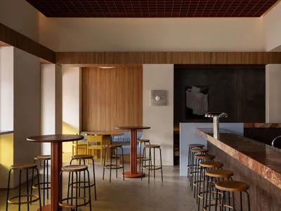 A modern restaurant bar with wooden tables and stools, featuring copper accents and a warm, inviting atmosphere.