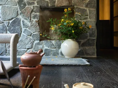 A cozy living room with a stone fireplace, wooden floor, and a white vase with yellow flowers.