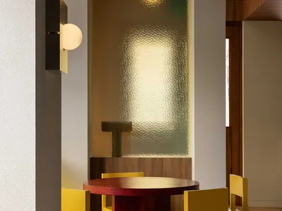 Modern restaurant interior featuring a wooden round table surrounded by yellow chairs.