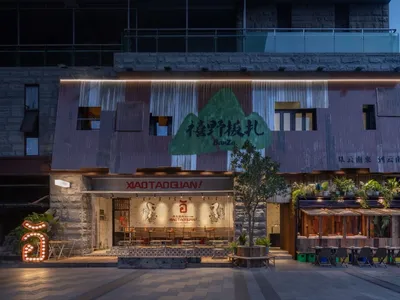 Modern restaurant exterior with metallic cladding, illuminated signage, and outdoor seating area.