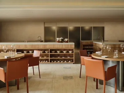 A modern restaurant interior featuring wooden furniture, concrete countertops, and glass elements.