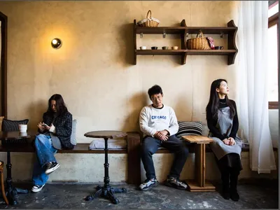 三人坐在舒適的咖啡廳內，搭配木質餐桌、布面坐墊、混凝土牆面與金屬家具。